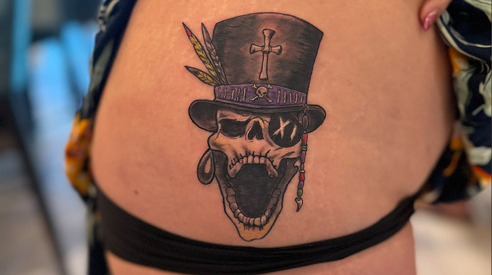 Tattoo of skull with top hat and cross, mouth open with patch on eye. Scratched in roman numerals in number 11