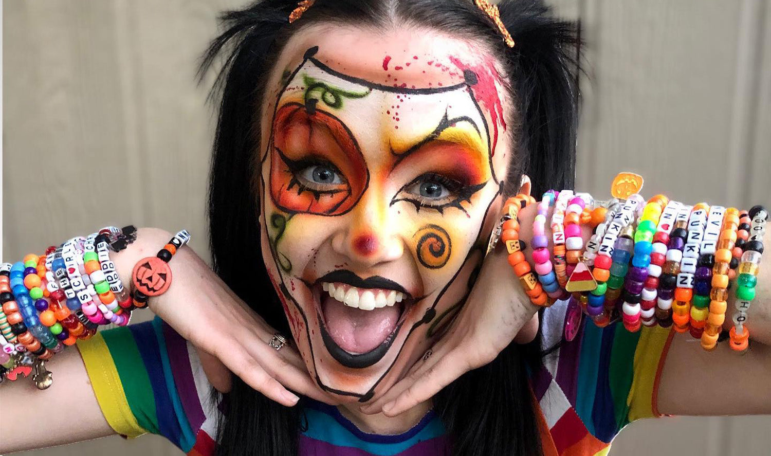 Woman smiling covered in face makeup wearing a lot of bead bracelets