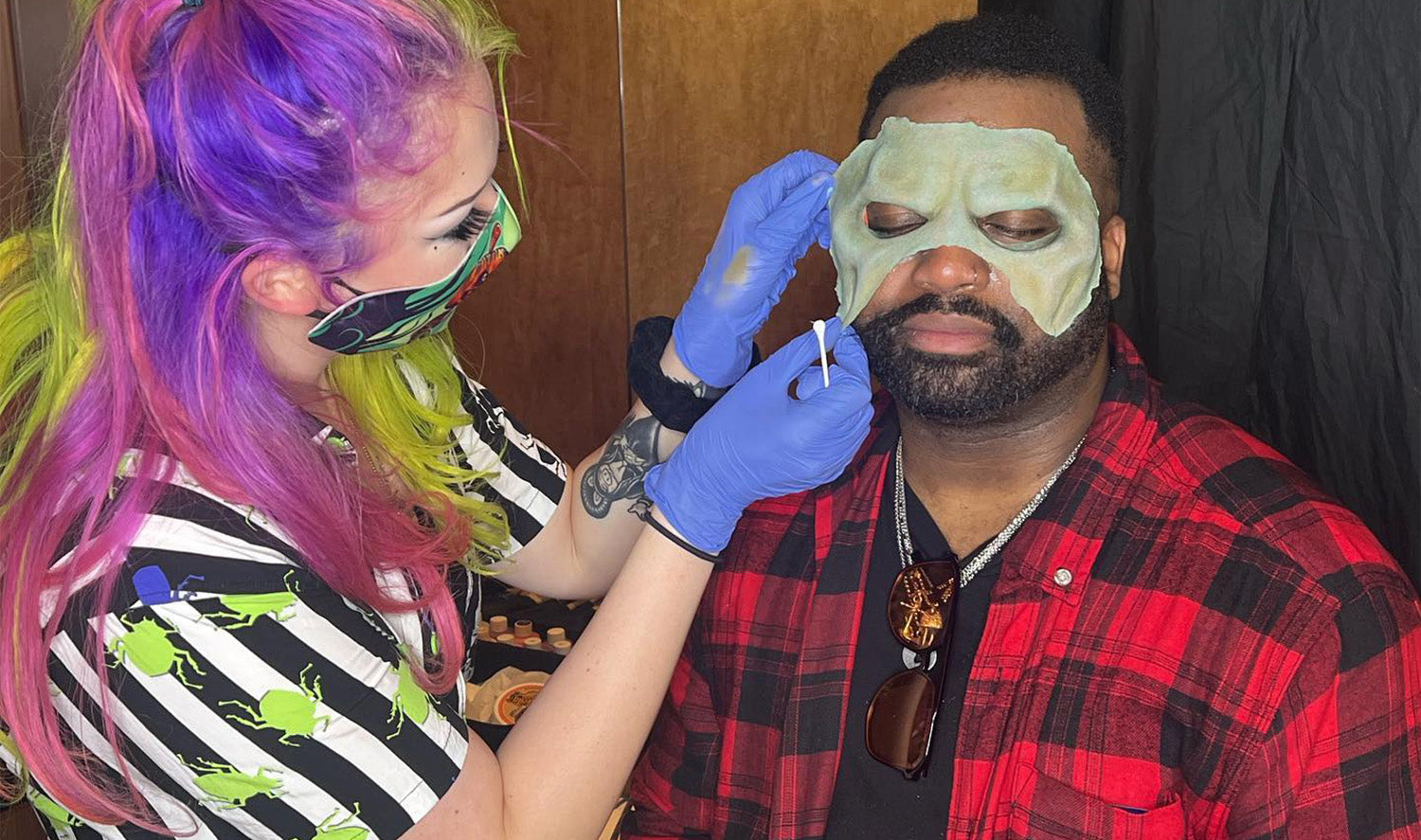 Artist in Beetlejuice shirt applying face makeup for costume to guest